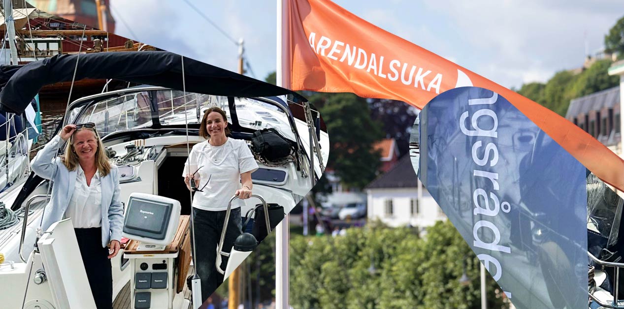 To personer står om bord på en båt under Arendalsuka. Den ene holder i rekkverket, mens den andre står ved styreposisjonen. I bakgrunnen vaier et oransje banner med teksten 'ARENDALSUKA'. Foto av Forskningsrådet og Arendalsuka/Mona Hauglid