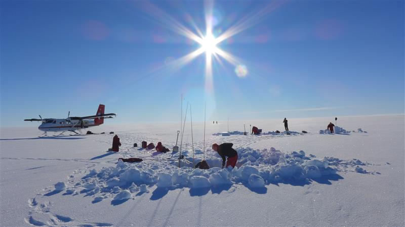 forskere som graver i isen i Antarktis, et fly i bakgrunnen, blå himmel