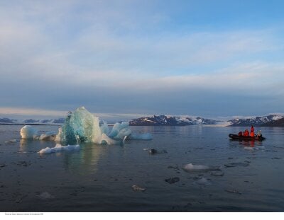 Researchers on dingy boat and an iceberg in the fjord