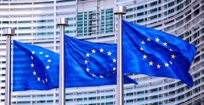 Tre EU-flagg vaiende i vind foran et stort kontorbygg