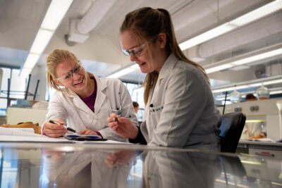 to kvinnelige studenter i hvite labfrakker i en lab