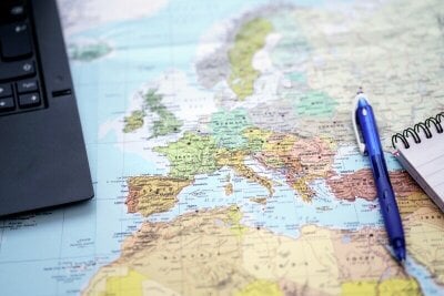 Skrivebordsunderlag med kart over Europa med del av laptop, penn og notatblokk oppå