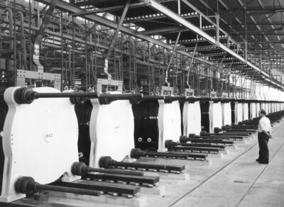 Inne i et fabrikkanlegg, en mann ser på en rekke med store og like installasjoner